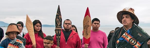Lummi leader and youth at Cherry Point bearing carved canoe paddles