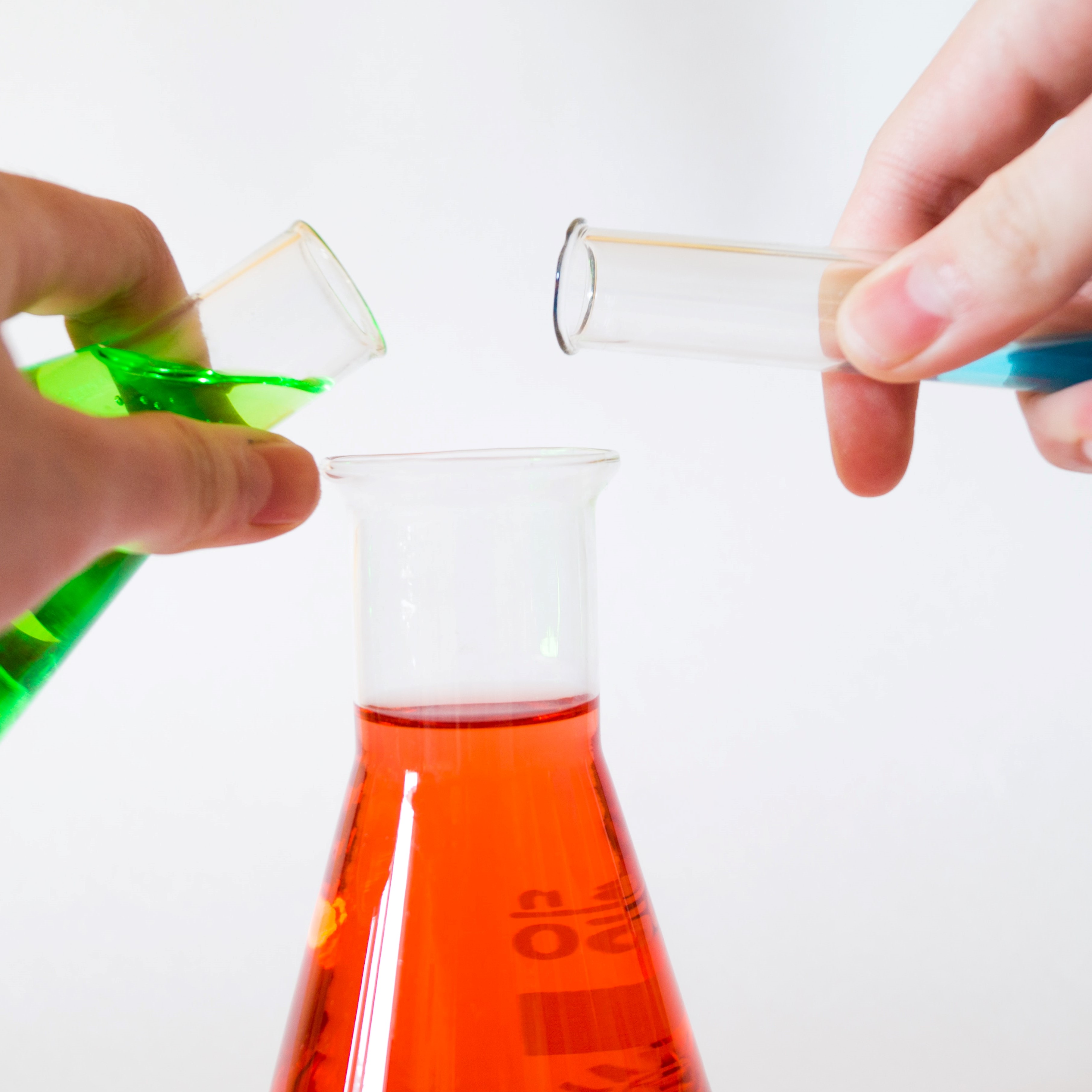 Hands pouring colored liquids into Erlenmeyer flask