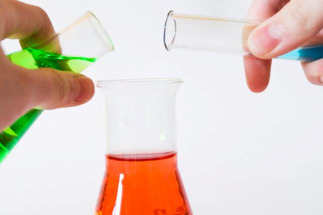 Hands pouring colored liquids into Erlenmeyer flask